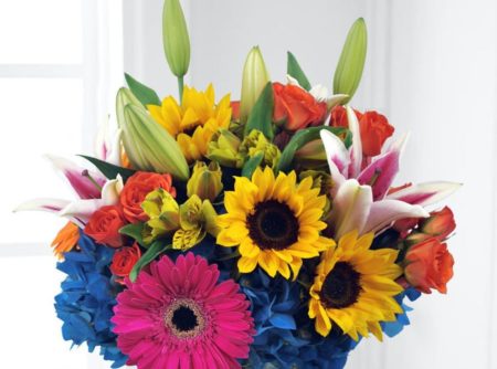 Eye-catching star gazer lilies unfold their petals amongst orange spray roses, hot pink gerbera daisies,yellow alstroemeria, and blue hydrangea with lush greens. Clustered in a glass vase, this vibrant bouquet is sure to express your happiest wishes